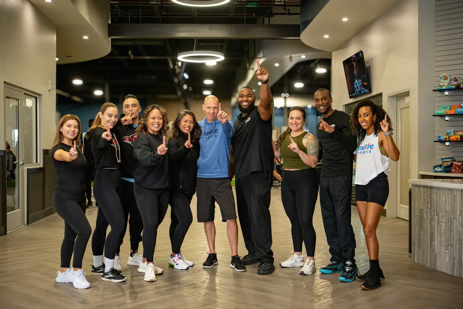 Ten Onelife Fitness team members smiling together inside the gym.